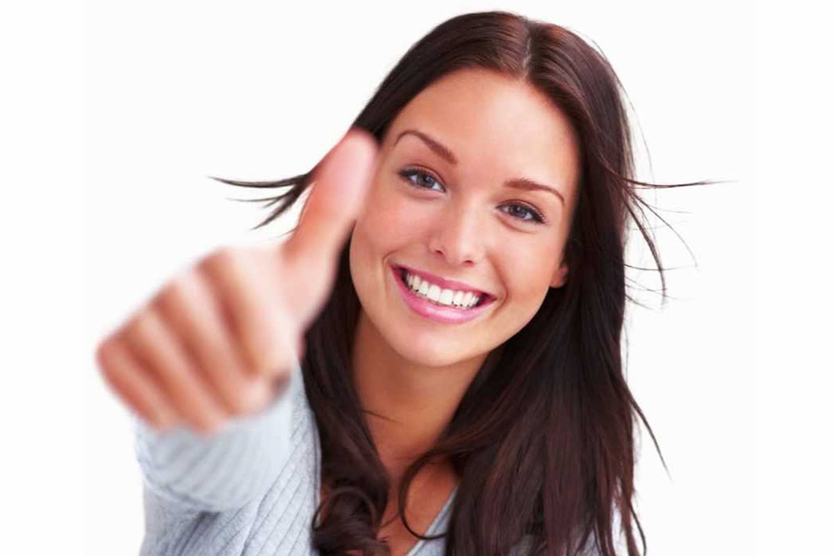 Woman smiling after teeth whitening, showing thumbs up